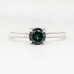 a white gold ring with a green diamond in the center and a thin band around it