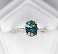 a ring with a blue diamond in it sitting on a white cloth covered box,