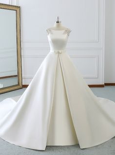 a white wedding dress on display in front of a large mirror with a gold frame