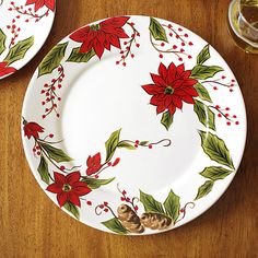 two plates decorated with holly and poinsettis on a wooden table next to wine glasses