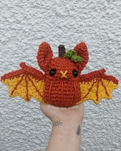 a hand holding up a small crocheted red and yellow bat with green leaves on its wings