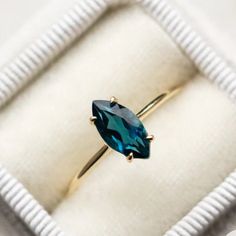 a ring with a blue stone in it on a white cloth box that is open