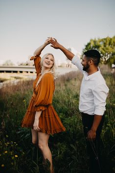 a man and woman standing in tall grass with their arms around each other's shoulders