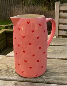 a pink pitcher sitting on top of a wooden table with hearts painted on the side