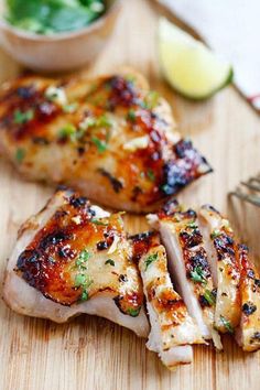 two pieces of chicken on a wooden cutting board next to a fork and small bowl