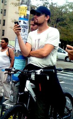 two men standing next to each other while looking at their cell phones on the street