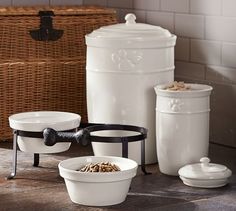 three white bowls with black handles are sitting on a table next to two large containers