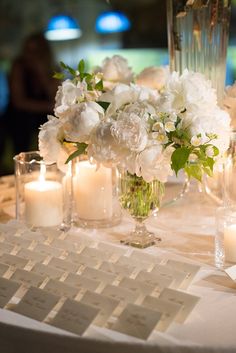 white flowers and candles on a table with place cards for guests to write in them