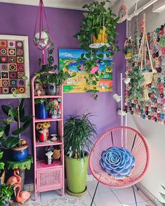 a room filled with lots of potted plants and hanging art on the wall next to a pink chair