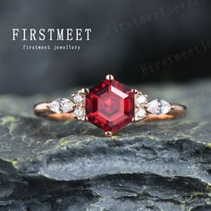 an engagement ring with a red stone surrounded by white diamonds on top of a rock