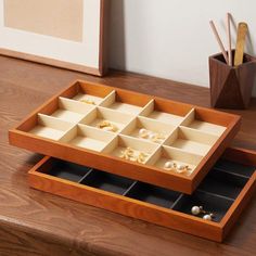 a wooden box with compartments filled with jewelry on top of a table next to a plant