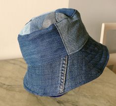 Blue jeans bucket hat. For him or her. This hat is made from upcykled blue denim. I sewn it on my lovely vintage sewingmachine. And yes, you can tell this item is handmade and quite unike.  It has a small  zipper pocket and several seams from the fabric, wich use to be trousers. The top of this hat is made from small patches. Inside has a cord in a canal in the lining Inside lining is from light lilac cotton. You can wash in machine, 40 celicius and iron the brim. The brim is sturdy enough to be a good sunscren, and soft enough to sleep comfy on the bus. This hat is a medium size, about 57-58 cm/22,8-23 inch, and it is totaly unike, like you! It is handmade by me, and labeled "carrot". The carrot label is for things I sew from upcykled fabrics, and stands for eco-friendly items.  It will b Blue Denim Bucket Hat With Short Brim, Denim Blue Cotton Bucket Hat With Curved Brim, Blue Denim Sun Hat With Curved Brim, Denim Blue Bucket Hat With Short Brim, Brimmed Cotton Hat In Denim Blue, Denim Blue Brimmed Cotton Hat, Blue Denim Bucket Hat, Cotton Brimmed Hat In Denim Blue, Denim Blue Bucket Hat