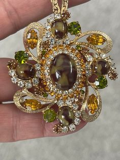 "Vintage Pendant Necklace made with topaz, olivine, and clear crystal rhinestones, and Art glass cabochons. 18\" in length, likely gold plated chain. Estimate era to be \"60's\"." Vintage Multi-stone Gold Brooches, Vintage Gold Multi-stone Brooches, Gold Crystal Jeweled Brooches, Retro Jeweled Gold Jewelry, Retro Gold Jeweled Jewelry, Gold Crystal Brooch Jewelry, Gold Crystal Jewelry With Brooch, Vintage Rhinestone Jewelry, Vintage Pendant Necklace