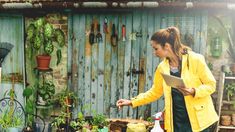 a woman standing in front of a table filled with plants and potted plants next to a building