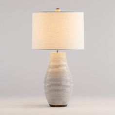 a white lamp with a beige shade on the base and a light bulb at the end