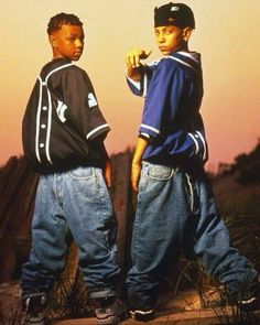 two young boys standing next to each other in front of a sunset and sand dune