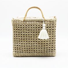 a woven wicker bag with a tasseled handle and white pom - pom