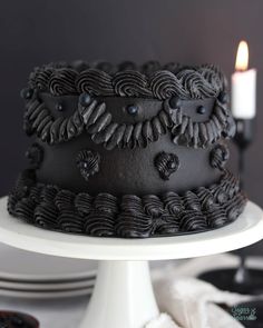 a chocolate cake on a white plate with a lit candle in the middle and black icing