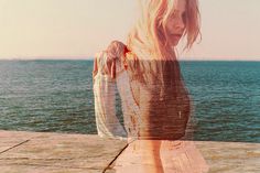 a woman standing on top of a pier next to the ocean with her hair blowing in the wind