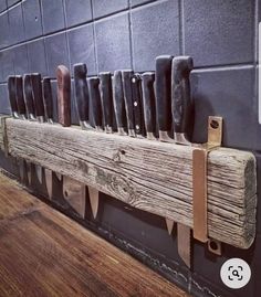 a bunch of knives are hanging on a wooden board in a room with tile walls