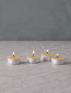 three small candles sitting next to each other on a marble counter top, with one burning in the middle