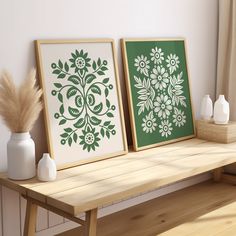 two green and white prints sitting on top of a wooden table next to vases