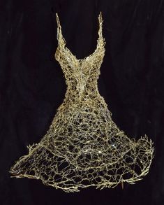 a dress made out of gold wire on a black background with the back turned to look like it is being woven