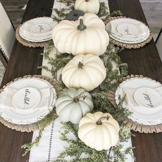 the table is set with white pumpkins, greenery and plates for dinner guests