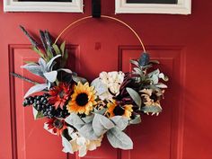 a wreath with sunflowers and other flowers hanging on a red door