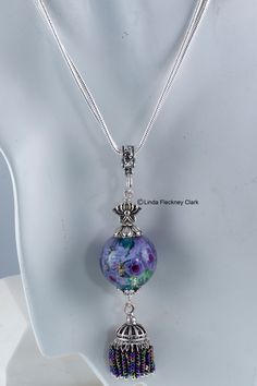 "I have created this one-of-a-kind 'Eastern Iris' pendant necklace from lampwork and dichroic round focal bead containing glass flowers, silver plated brass and bead tassel, silver plated pewter lotus bead, silver plated brass and pewter bead caps, bale and jewellery wire, silver plated brass double snake chain with lobster clasp Alt Text Necklace of lampwork and dichroic round focal bead of glass flowers, silver plated brass and bead tassel, silver plated pewter lotus bead, silver plated brass Silver Czech Glass Round Necklace, Silver Glass Flower Pendant Jewelry, Silver Murano Glass Necklace For Jewelry Making, Round Silver Czech Glass Necklace, Silver Murano Glass Round Necklace, Artistic Silver Jewelry With Round Beads, Adjustable Silver Murano Glass Necklace, Silver Murano Glass Round Pendant Necklace, Silver Murano Glass Round Pendant Jewelry