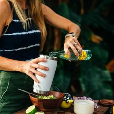 a woman pouring something into a cup on top of a wooden table next to other food items