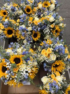 a bunch of sunflowers and other flowers are arranged in a box on the ground