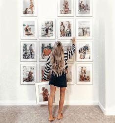 a woman standing in front of a wall with pictures on it and holding up her hand