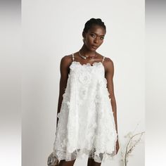 a woman standing in front of a white wall wearing a dress with flowers on it