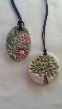 two necklaces with flowers on them sitting on top of a white cloth covered table