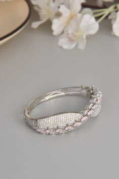 Embrace the soft elegance of our Blush Bloom Bracelet, a delicate ode to feminine beauty. Crafted from durable brass and adorned with shimmering CZ stones, this bracelet captures the essence of grace and sophistication. Finished in radiant rhodium, the gentle pink CZ stones evoke the tender bloom of spring flowers, infusing your look with a touch of natural charm. Each stone radiates with a subtle sparkle, casting a luminous glow that captivates the senses. Let this exquisite bracelet grace your Elegant Pink Diamond Bracelet With Diamond Accents, Elegant Diamond Bracelets For Promise, Formal Pink Bracelets With Diamond Accents, Silver Bracelet With Cubic Zirconia Stones, Glamorous Bangle Jewelry Gift, Glamorous Bangle Jewelry For Gifts, Elegant Bangle With Sparkling Stones, Feminine Wedding Jewelry Bangle, Elegant Promise Bracelet Jewelry