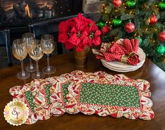 the table is set for christmas with wine glasses and napkins on it, next to a potted christmas tree