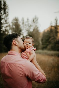 a man holding a baby in his arms and looking at the sky with trees in the background