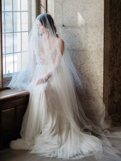 a woman in a wedding dress sitting on a window sill looking out the window