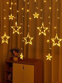 some white stars hanging from the ceiling in front of a curtain with lights on it