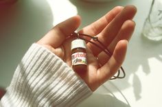 a person holding an essential oil bottle in their left hand, on a white table