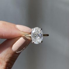 a woman's hand holding an engagement ring with a diamond in the middle, on top of her finger