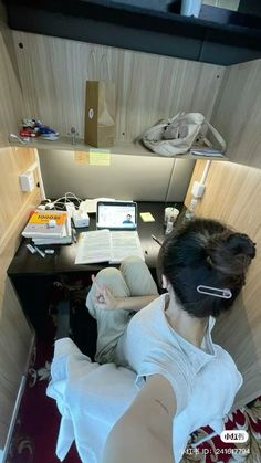 a woman sitting at a desk in an office cubicle with a laptop and books on it