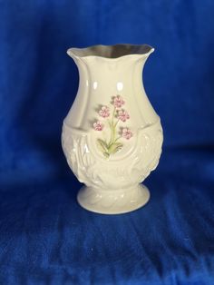 a white vase with pink flowers painted on the bottom and sides, sitting on a blue background