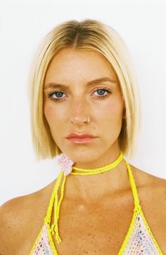 a woman with blonde hair wearing a yellow halter top and pink flowers on her neck