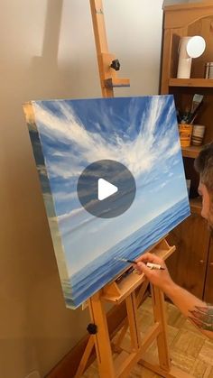 a man is painting clouds on an easel