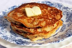 a stack of pancakes on a blue and white plate topped with butter, sitting on a table