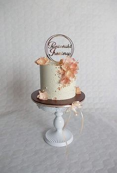 a white and brown wedding cake with flowers on the top is sitting on a pedestal