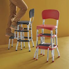 a man standing on top of three stools in front of a yellow wall with red and black seats