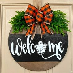 a welcome sign hanging on the front door with a pumpkin wreath and plaid bow around it